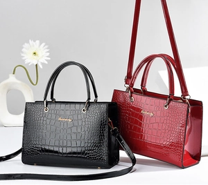 Detail view of glossy crocodile pattern patent leather handbag with gold metal logo