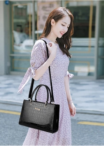 Detail of black crocodile texture handbag with gold logo held by a model in floral dress