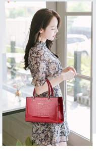 Detail of red croc-embossed patent leather handbag with golden metal logo and dual handles