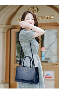 Detail of dark blue crocodile texture handbag with adjustable shoulder strap worn by model