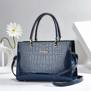 Dark blue crocodile pattern handbag with gold hardware and shoulder strap on white backdrop