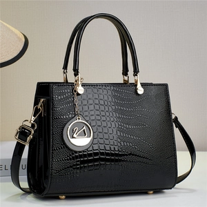 Close-up of black lizard pattern glossy leather handbag with gold hardware and charm