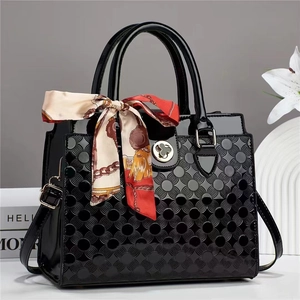 Détail du sac en cuir verni noir gaufré avec fermoir trèfle doré et foulard en soie