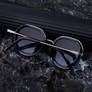 Detail of oval sunglasses with thick black frame and silver metal temples on black rock