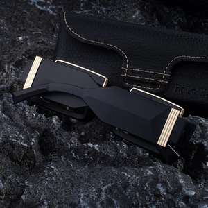 Close-up of matte black square sunglasses with gold accents on a textured rock surface
