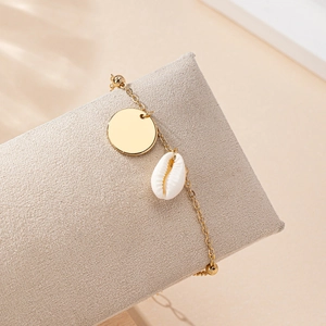 Bracciale dorato con ciondoli a conchiglia e cerchio su supporto per gioielli beige