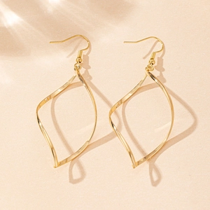 Gros plan de boucles d'oreilles géométriques torsadées dorées sur fond texturé neutre