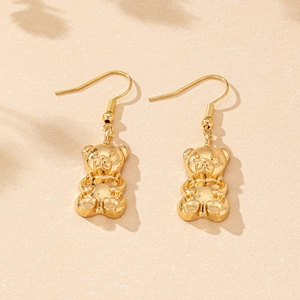 Detailed view of polished golden 3D teddy bear earrings on textured sandy background