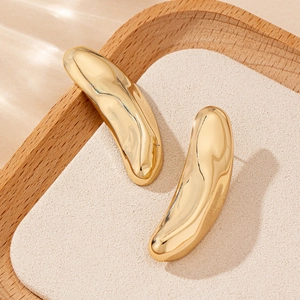 Detailed close-up of bean-shaped gold metal stud earrings on a wooden display tray