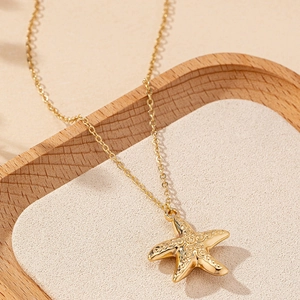 Elegant gold starfish pendant necklace with detailed texture on a beige display tray