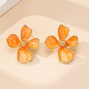 Détails macro des boucles d'oreilles fleur en émail orange et finitions dorées
