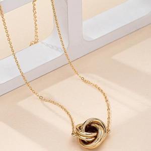 Elegant gold-tone twisted interlocked triple ring pendant necklace on a geometric display