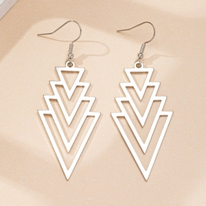 Detailed close-up of layered silver triangle drop earrings on beige textured background