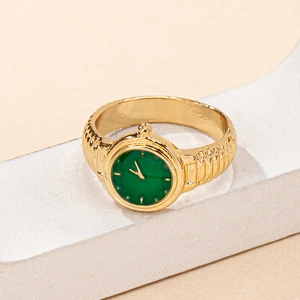 Close-up of golden watch ring with green dial and textured metal band on white stand