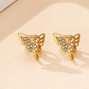 Detailed close-up of gold butterfly ear clips with sparkling rhinestones on beige texture