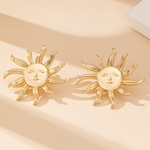 Macro shot of gold sun face earrings with rays on a minimalist beige background