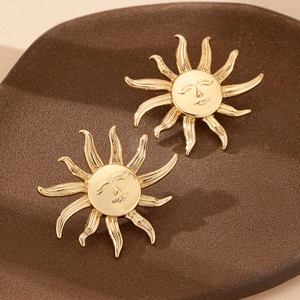 Elegant gold sun god face stud earrings with sunburst rays on dark textured background