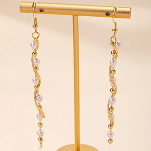 Détail de longues boucles d'oreilles spirales dorées avec perles sur un support
