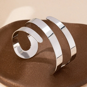 Minimalist silver spiral open bangle with polished mirror finish on a rustic tray