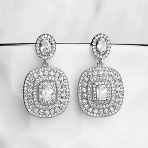 Close-up of tassel earrings with shimmering zircons hanging on a white porcelain cup