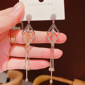 Gros plan de boucles d'oreilles dorées géométriques avec cristaux et franges longues