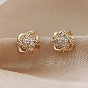 Gros plan de boucles d'oreilles trèfle dorées avec zircons sur fond de soie rose pâle