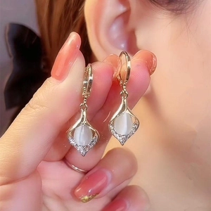 Vue rapprochée de boucles d'oreilles feuille dorée avec pierres œil de chat blanches