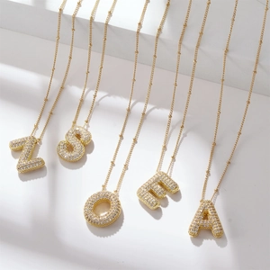 Golden cubic zirconia paved bubble letter pendants on bead chains over white steps