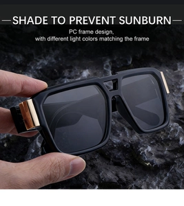 Close-up of black square sunglasses with gold metal hinge detail and grey lenses
