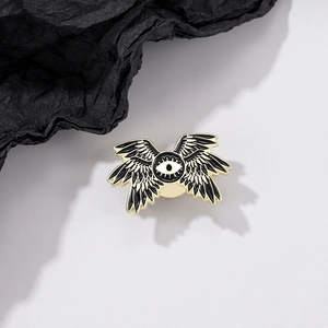 Detail of a dark fantasy enamel eye brooch with multiple black wings and gold plating