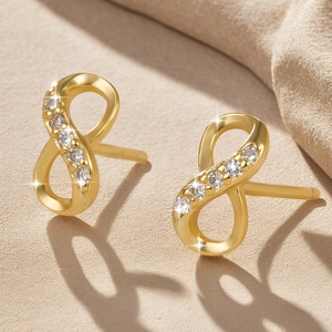 Golden infinity stud earrings featuring zircon accents on a warm textured backdrop
