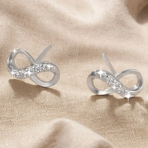 Sparkling infinity symbol stud earrings with zircons on elegant champagne silk fabric