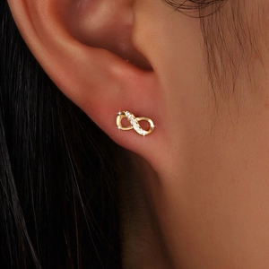Elegant gold infinity stud earrings with sparkling zircon stones worn on ear