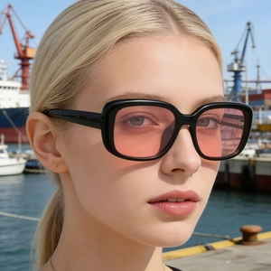 Fashionable square black sunglasses with pink lenses worn by a model at a port