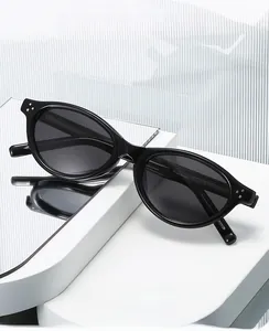Detail of oval black sunglasses with silver rivet accents on a reflective white pedestal
