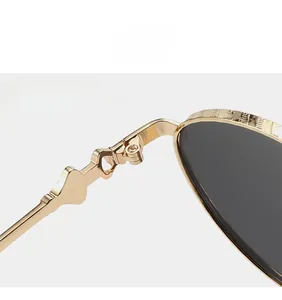 Close-up of golden metal hinges with intricate floral engraving on oval sunglasses