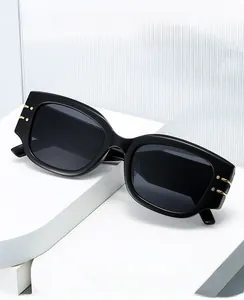 Detail view of black rectangular sunglasses with golden metal accents on minimalist stand