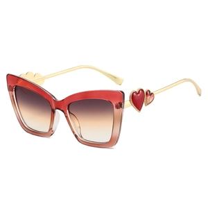 Cat-eye zonnebril met rood kleurverloop montuur en gouden hartjes op de metalen pootjes