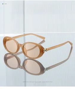 Detail of oval amber sunglasses with golden sphere hinge on a reflective glass surface
