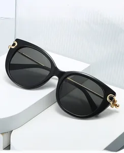 Detail of cat eye sunglasses with golden C-shaped metal accents on white geometric base