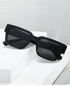 Détail de lunettes de soleil carrées noires avec branches larges sur support blanc épuré