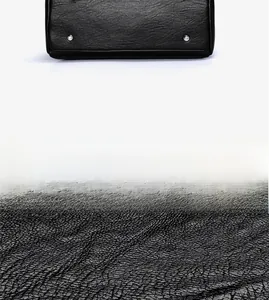 Close-up of black lychee grain leather texture and metal bottom studs on a tote bag