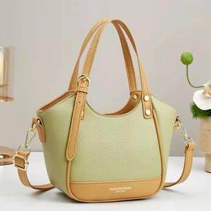 Green and tan leather tote bag with tassels and shoulder strap on a white surface