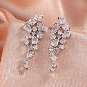 Détail de boucles d'oreilles pendantes argentées avec zircons sur soie champagne