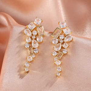 Détail de boucles d'oreilles pendantes dorées serties de zircons sur fond de satin