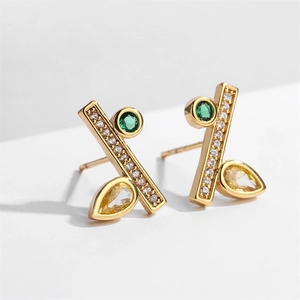 Vue macro de boucles d'oreilles dorées géométriques avec gemmes vertes et jaunes