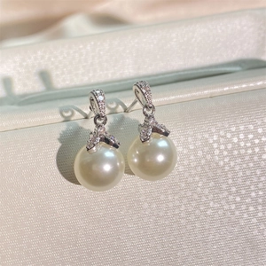Detail view of pearl earrings with curved zircon-set hooks on a luxury display stand