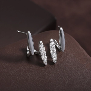 Macro detail of curved silver earrings with sparkling cubic zirconia on a leather background