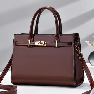 Sac à main en cuir verni marron foncé avec fermoir doré dans un décor minimaliste