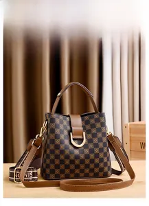 Détail d'un sac seau à motif damier avec poignées en cuir marron et boucles dorées